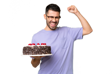 Young caucasian man holding birthday cake isolated on green chrome background celebrating a victory
