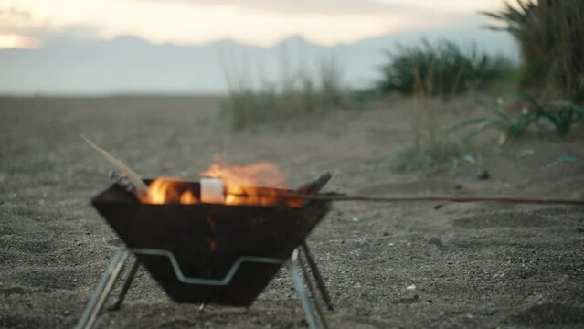 A girl in a red Santa hat is frying marshmallows on the beach by the sea. Christmas on the background of mountains.
