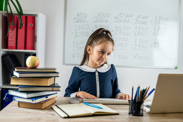 Smiling little schoolgirl posing taking notes and sitting looking at camera.