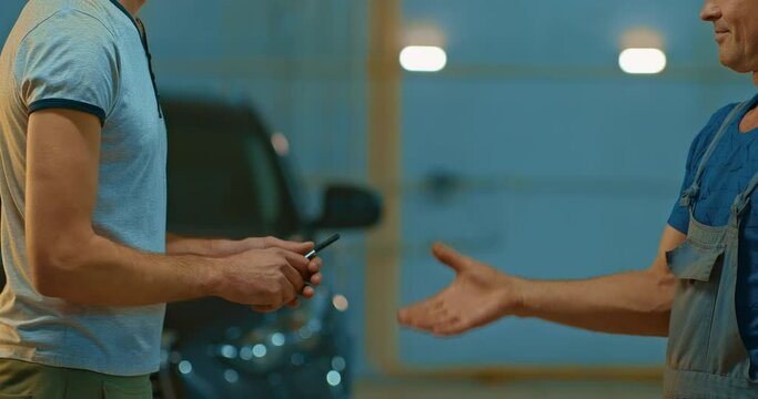 Car mechanic passes the keys to the customer from his car. Satisfied customer at a car dealership. Handshake. close-up.