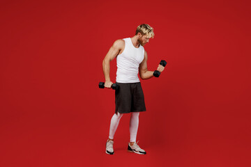 Full size side view powerful young strong sporty toned sportsman man wearing white clothes spend time in home gym hold dumbbells posing isolated on plain red background Workout sport fit body concept.