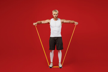 Full body young strong sporty toned sportsman man 20s wearing white clothes spend time in home gym use rubber band expander for hands isolated on plain red background. Workout sport fit body concept.