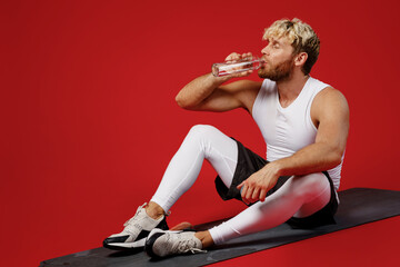Fototapeta na wymiar Full body sideways young strong sporty toned sportsman man wear white clothes spend time in home gym hold bottle drink water take break isolated on plain red background Workout sport fit body concept
