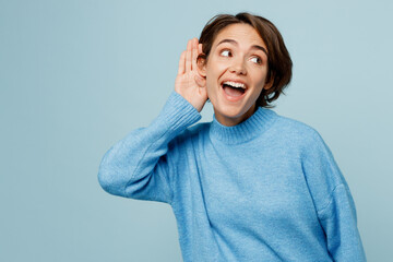 Young curious nosy fun caucasian woman wear knitted sweater try to hear you overhear listening intently isolated on plain pastel light blue cyan background studio portrait. People lifestyle concept.