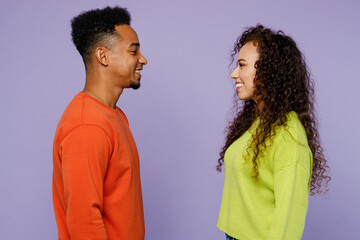 Side view smiling happy fun young couple two friends family man woman of African American ethnicity wearing casual clothes together look to each other isolated on pastel plain light purple background.