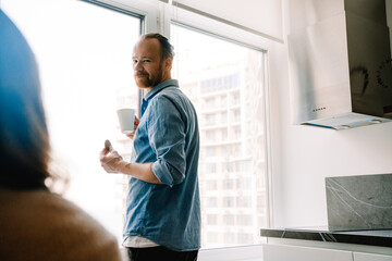 Obraz premium Young white bearded man wearing shirt drinking tea by window at home