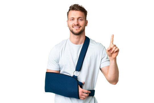 Young caucasian man with broken arm and wearing a sling over isolated chroma key background showing and lifting a finger in sign of the best
