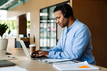 Fototapeta premium Indian businessman in headphones working on laptop computer in office