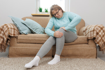 Mature woman suffering from knee ache on sofa