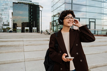 European woman in headphones using cellphone while standing on stairs