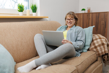 Technology, old age and people concept - happy senior woman in glasses with laptop computer and glass of wine at home