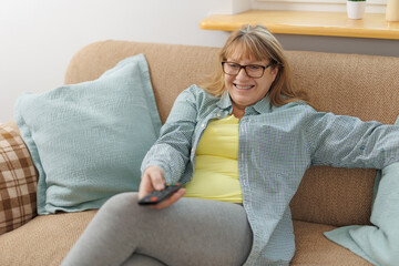 Obraz premium Mature blond woman watching television on sofa, in living room.