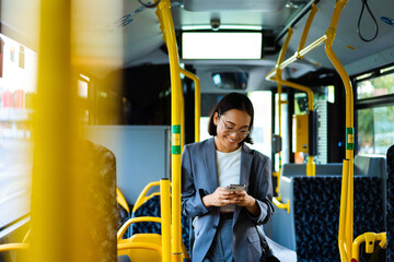 Asian woman smiling and using smart phone while standing in a bus