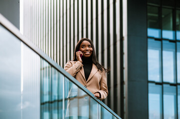 Young black woman talking on cellphone while standing by building