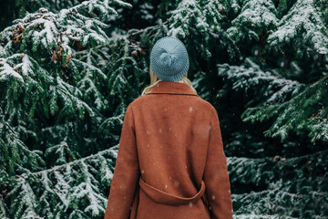 Woman wearing warm clothing in front of fir tree with snow