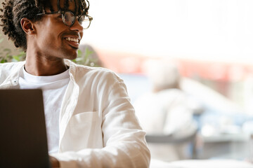 Obraz premium Young african american man smiling and using laptop in cafe indoors