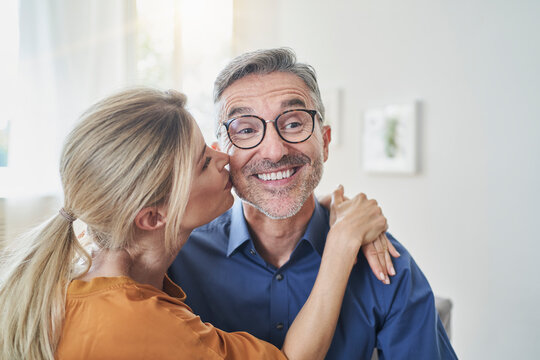 Woman kissing happy man at home