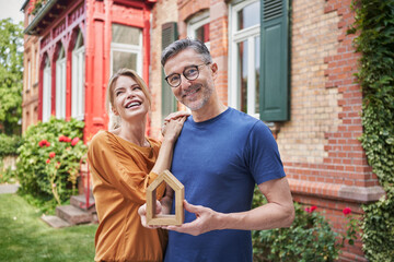 Happy woman standing by man holding house model in back yard