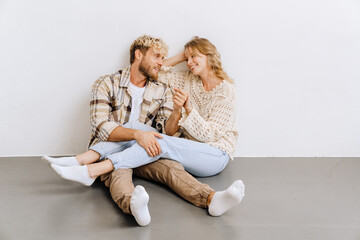 Obraz premium Joyful couple holding hands while sitting on the floor isolated