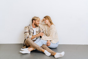 Young joyful couple holding hands while sitting on the floor isolated