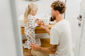 Fototapeta premium Young father helping his little daughter to clean her teeth in bathroom
