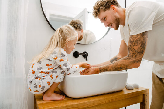 Young father helping his little daughter to wash her hands in bathroom