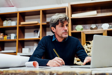 Mature man sketching in front of laptop at workshop