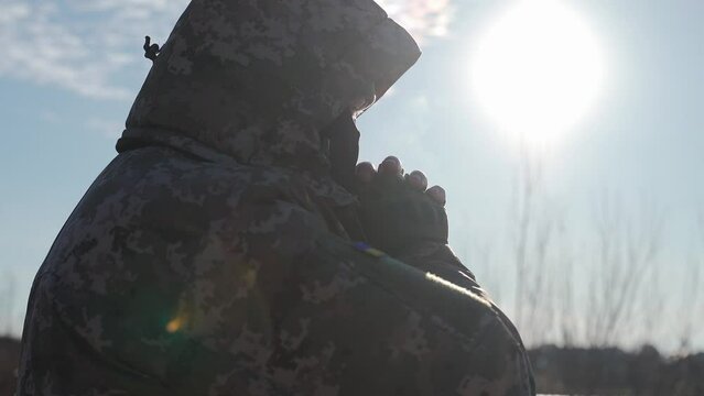Ukrainian military man warms his hands with his breath on a cold winter morning. the officer at the post is warming up. war in winter winter military uniform. military service at sub-zero temperatures