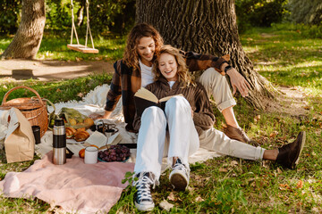 Young couple enjoying picnic time while reading a book under the tree in park