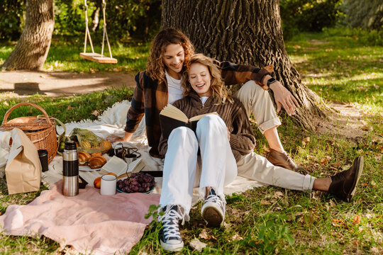 Young couple enjoying picnic time while reading a book under the tree in park