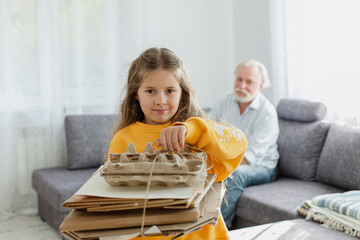 Girl carrying bunch of waste paper at home