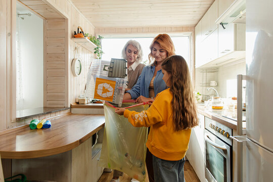 Grandmother, mother and daughter sorting recycling waste in kitchen