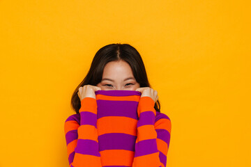 Asian girl hiding face in her t-shirt isolated over yellow background