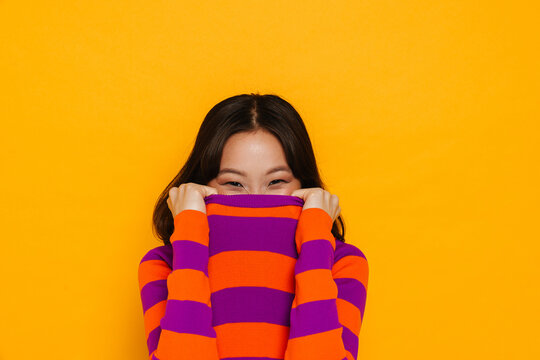 Asian girl hiding face in her t-shirt isolated over yellow background