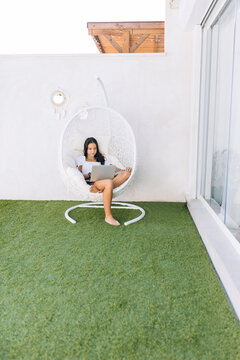 Girl using laptop sitting on hanging chair at backyard