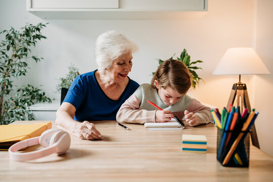 Smiling grandmother helping girl in study on table at home