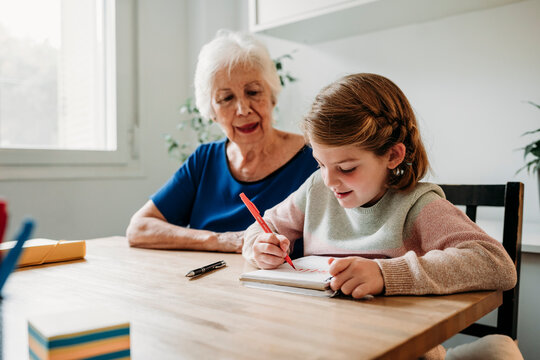 Grandmother helping girl in study on table at home