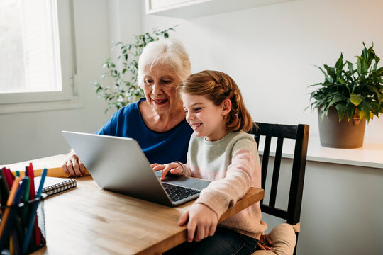 Grandmother helping granddaughter e-learning through laptop at home