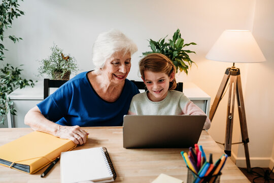 Smiling senior woman helping granddaughter studying through laptop on table at home