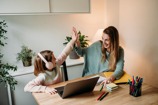 Happy mother giving high-five to daughter sitting with laptop at table