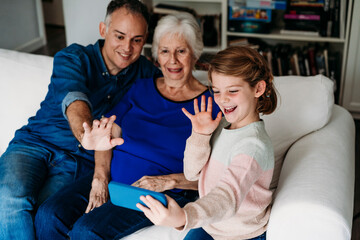 Happy girl with grandmother and father having video call on mobile phone at home