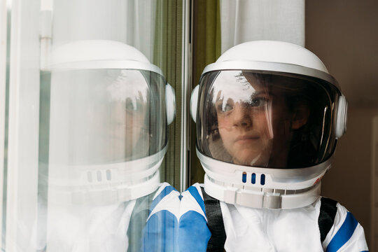 Thoughtful girl wearing space costume looking through window at home