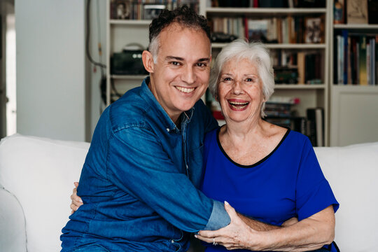 Smiling Son Embracing Happy Mother On Sofa At Home