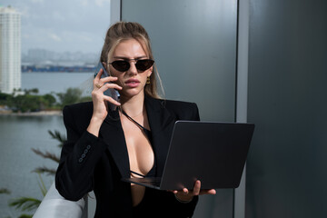 Sexy confident busines swoman in fashion business suit using laptop in office balcony view. Young female director, startup business, own online business.