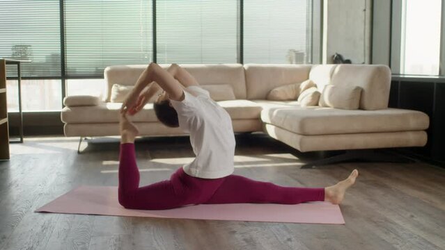 Middle age woman in sporstwear practicing yoga on red fitness mat in living room. Sporty Female making stretching the body on yoga mat at home. Healthcare and exercise mental therapy at home concept.