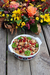 Cabbage pudding is a classic Swedish dish. An oven dish filled with cabbage and minced meat. In the background is a beautiful flower arrangement. The photo is taken on a wooden board.
