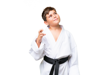 Little caucasian kid doing karate over isolated chroma key background with fingers crossing and wishing the best