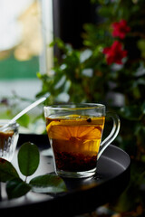 Glass cup of hot black tea lemon on dark background  with steam near window, cozy warm, relaxing.