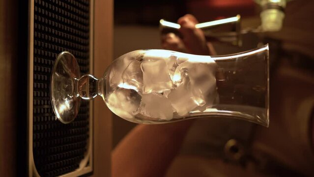 Barman pour gin into a glass with ice in bar.