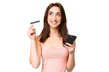 Young caucasian woman over isolated chroma key background buying with the mobile with a credit card while thinking